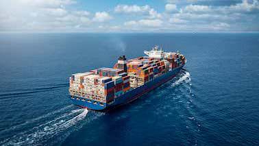 Aus der Vogelperspektive ist ein voll beladenes Containerschiff auf dem offenem Meer zu sehen.