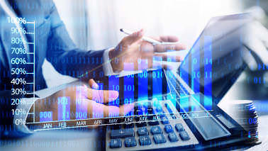 Ein Mann im Anzug gestikuliert mit einem Stift und einem Smartphone in den Händen an einem Laptop. Es sind nur seine Unterarme und das Laptop zu sehen, im Vordergrund liegt ein Taschenrechner. Das Bild wird von einem Diagramm mit leuchtend blauen Balken überlagert.